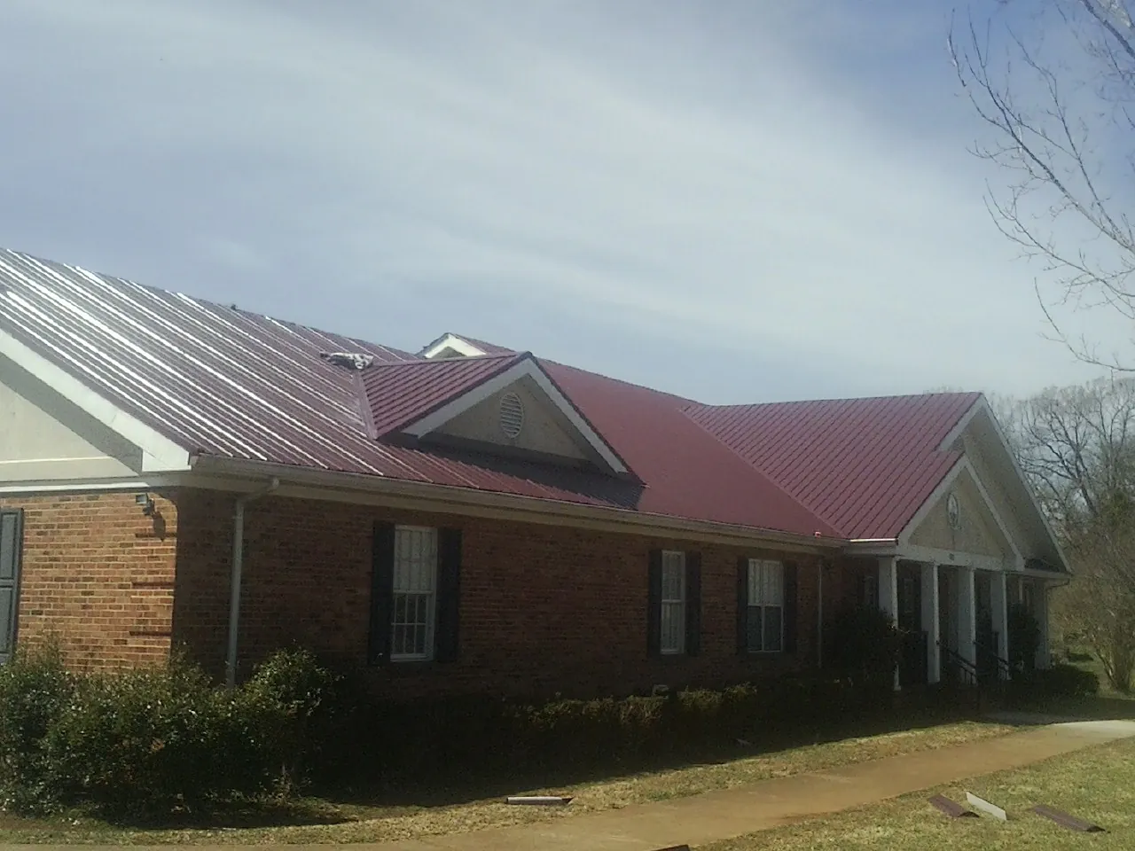 Red metal roof with gabled entries on a long brick building, from a Hail Damage Roof Repair job in Saint John
