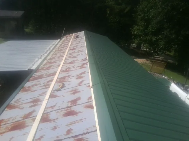 Old rusted panels beside newly installed green metal roofing — Wind Damage Roof Repair by Roofing Brothers in Saint John